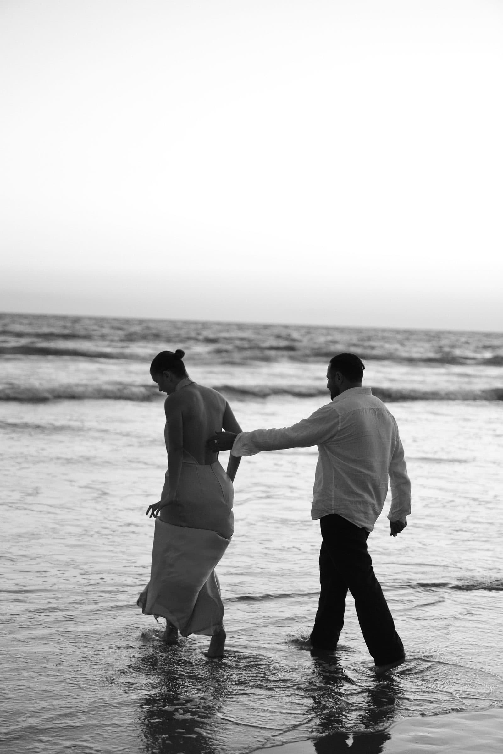 A couple walking together at the water’s edge, photographed in black and white
