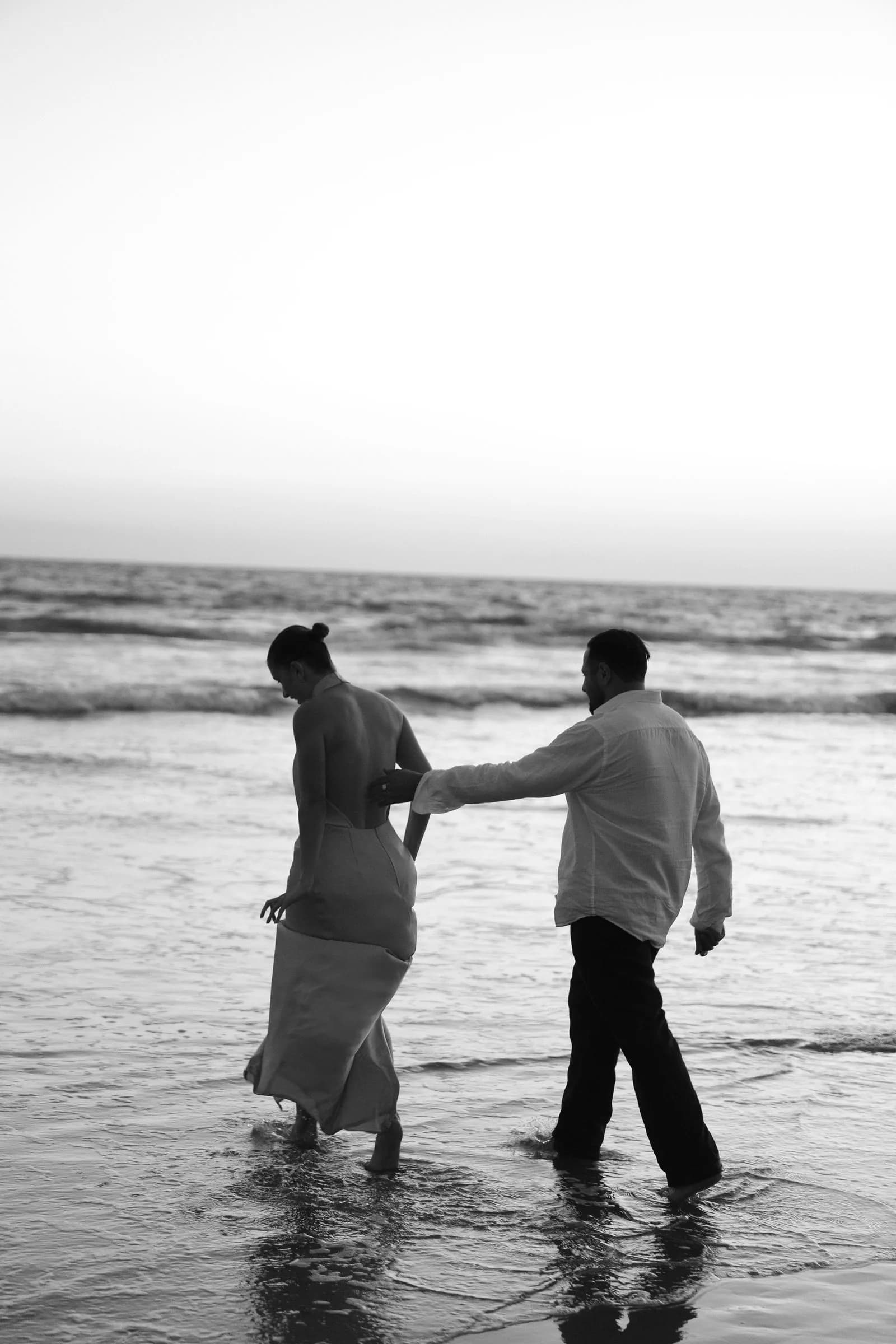 A couple walking together at the water’s edge, photographed in black and white